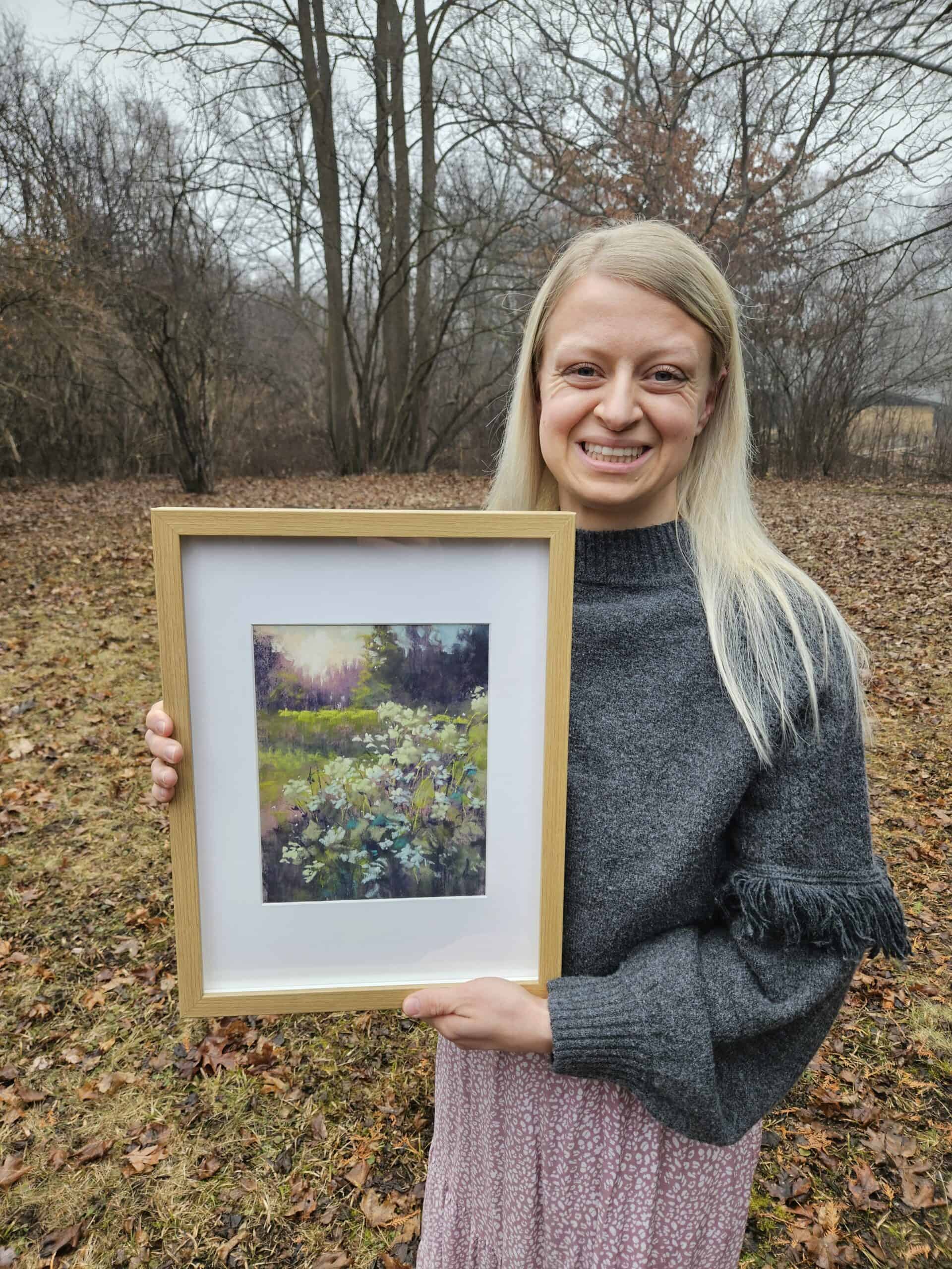 Josie holding a framed soft pastel landscape