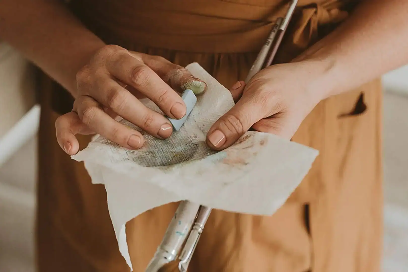 Valerie McKeehan's hands holding a soft pastel stick wrapped in paper.